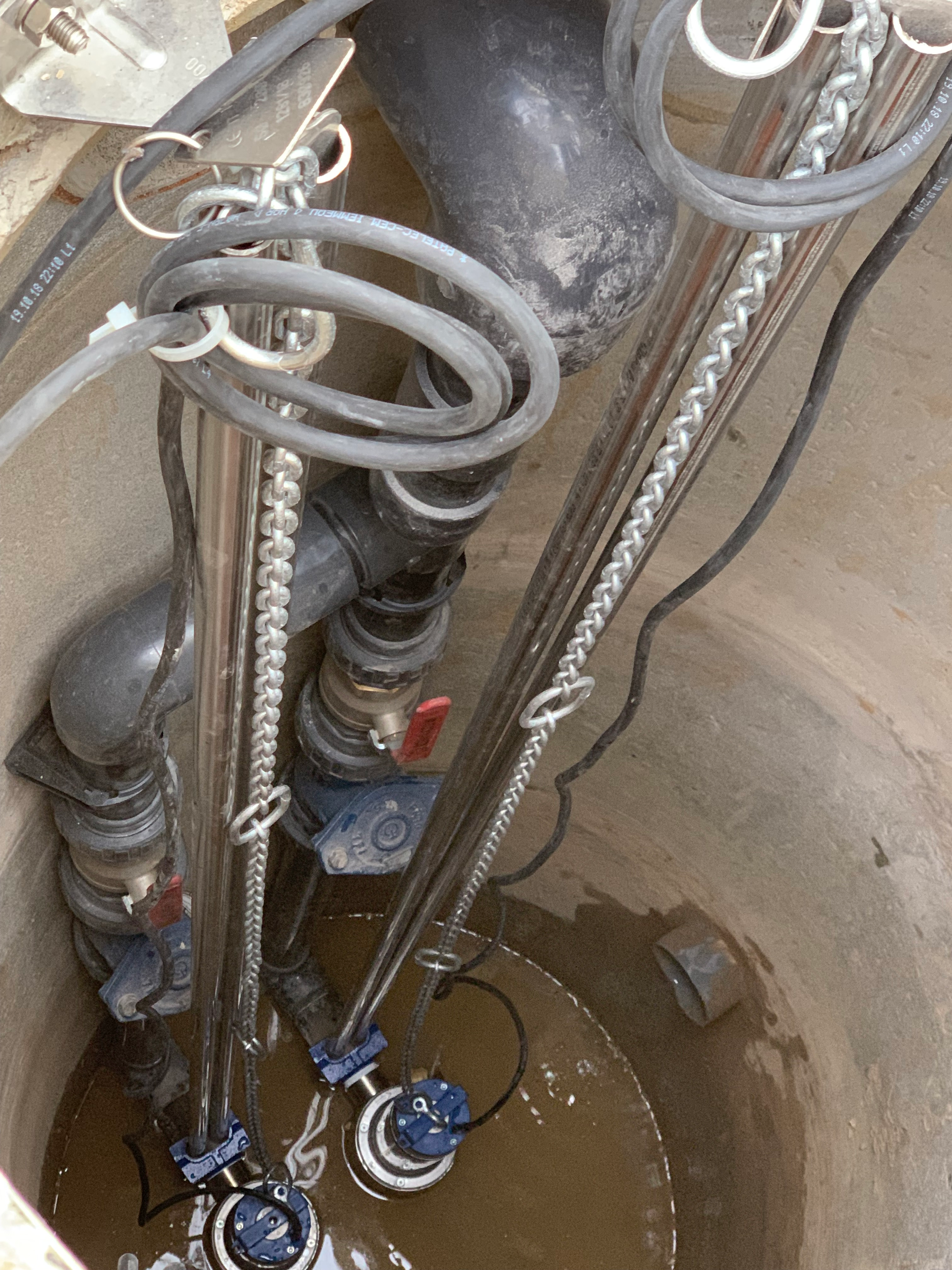 Un regard d'égout avec beaucoup de tuyaux et de fils qui en sortent.