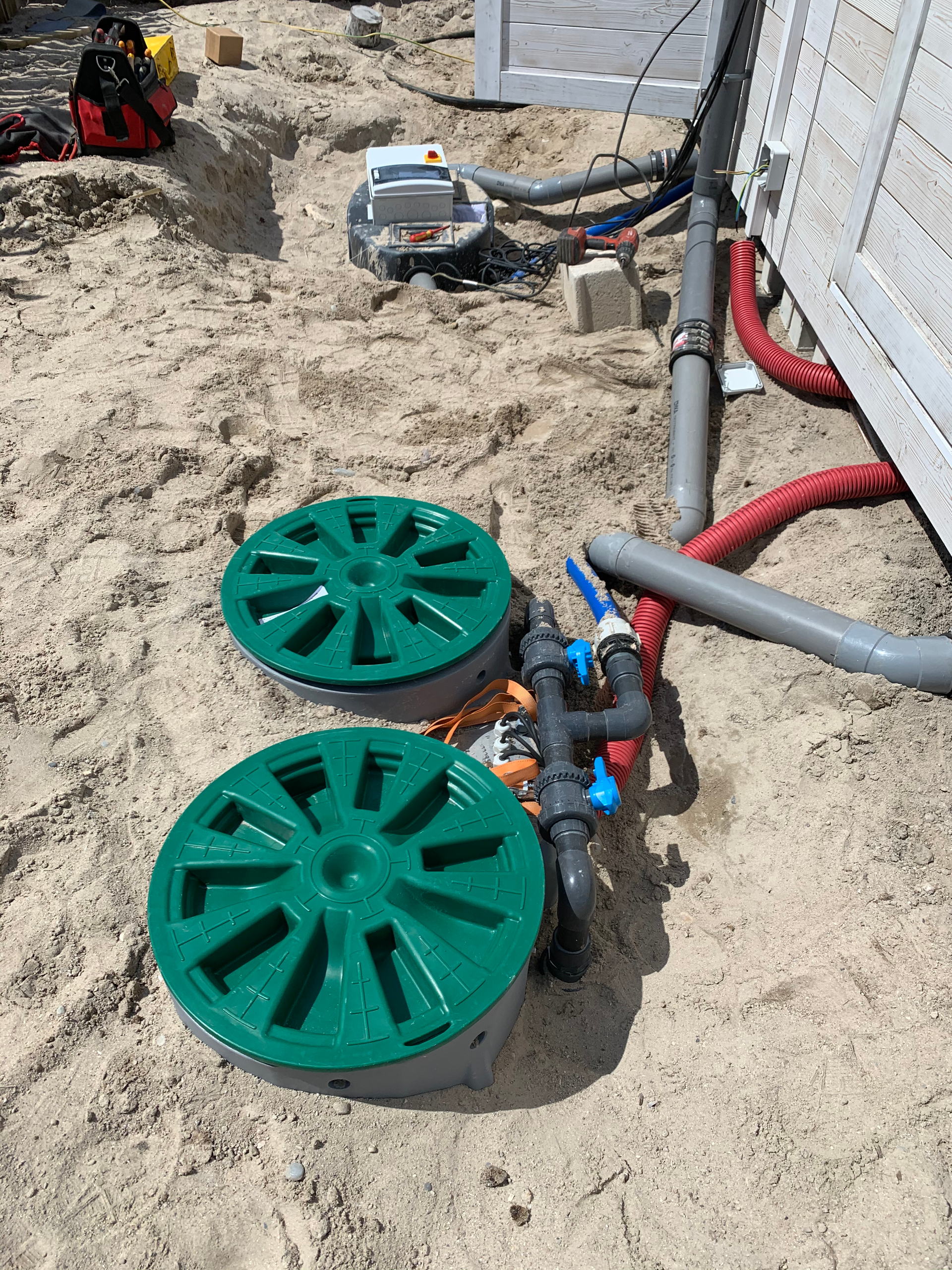 Deux couvercles de drain verts sont posés dans le sable à côté des tuyaux.