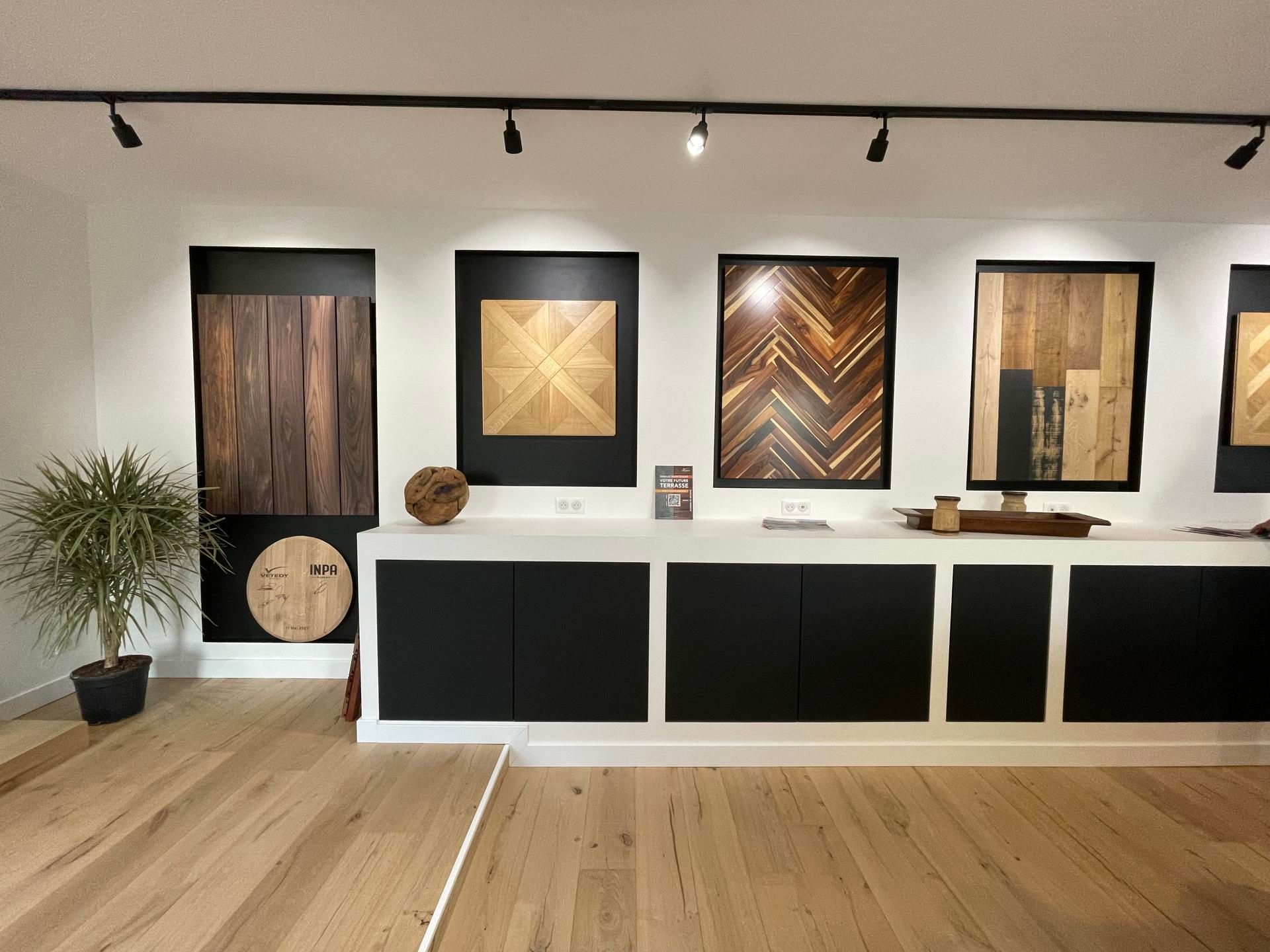 Des échantillons de parquet sont présentés sur des armoires blanches à cadres foncés, fixées au mur. Une petite plante se trouve à gauche.