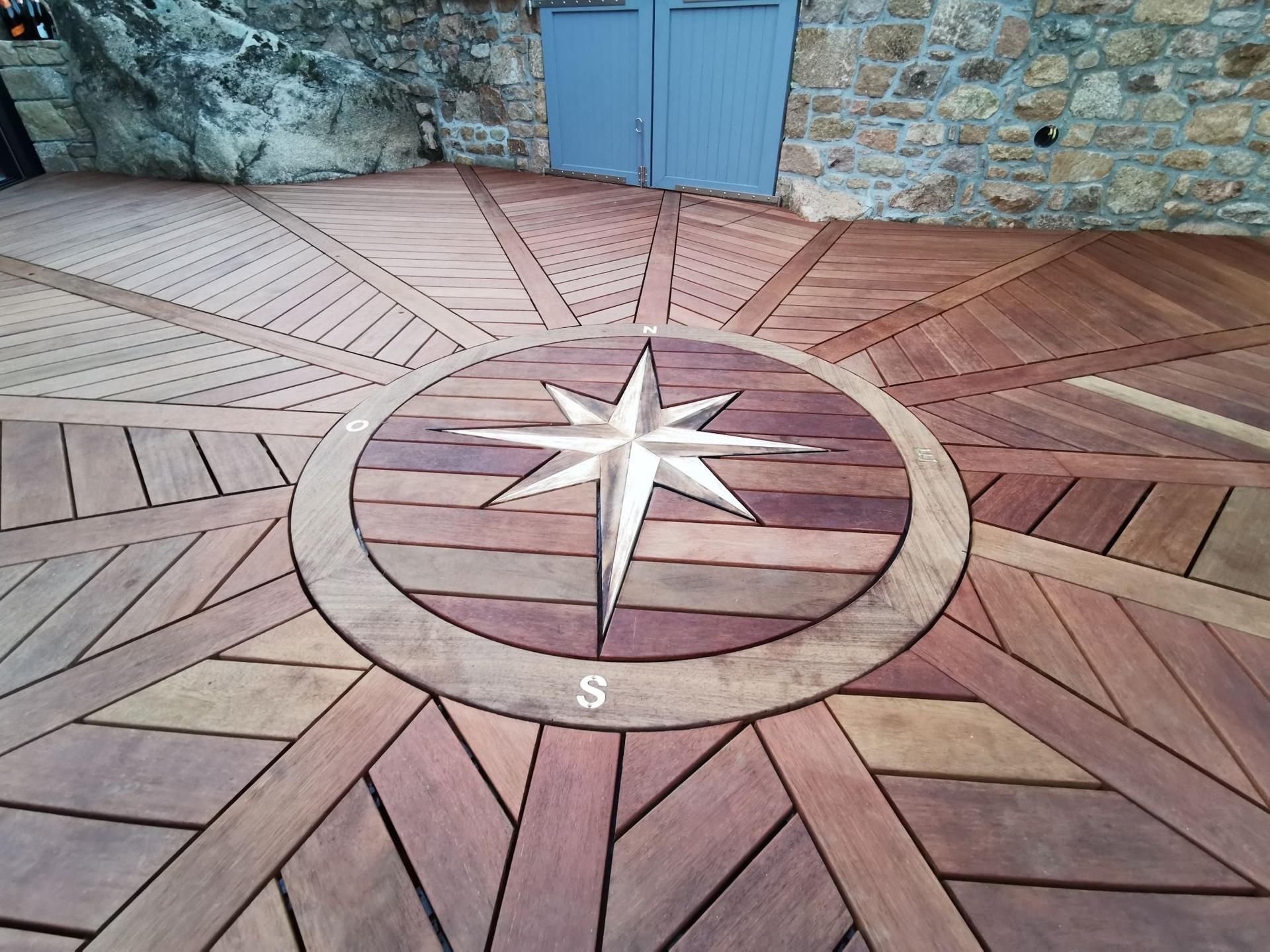 Terrasse en bois ornée d'une rose des vents et bordée de divers motifs géométriques.
