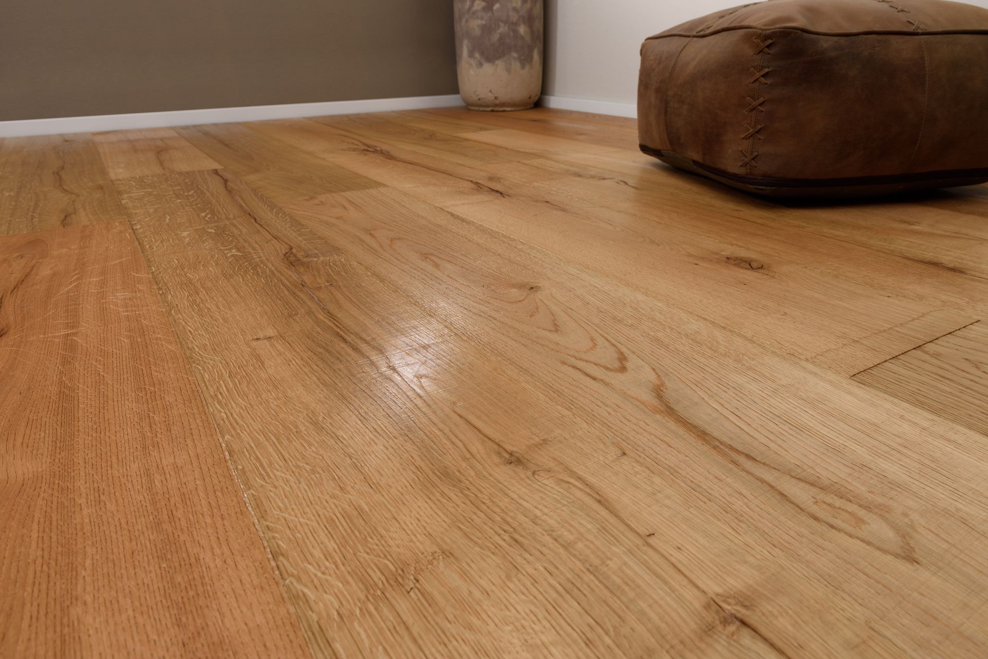 Plancher en bois massif avec un pouf en cuir marron en arrière-plan.