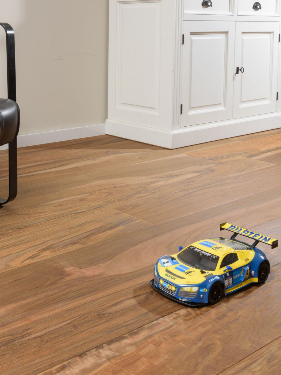 Voiture de course miniature sur parquet devant un meuble blanc.