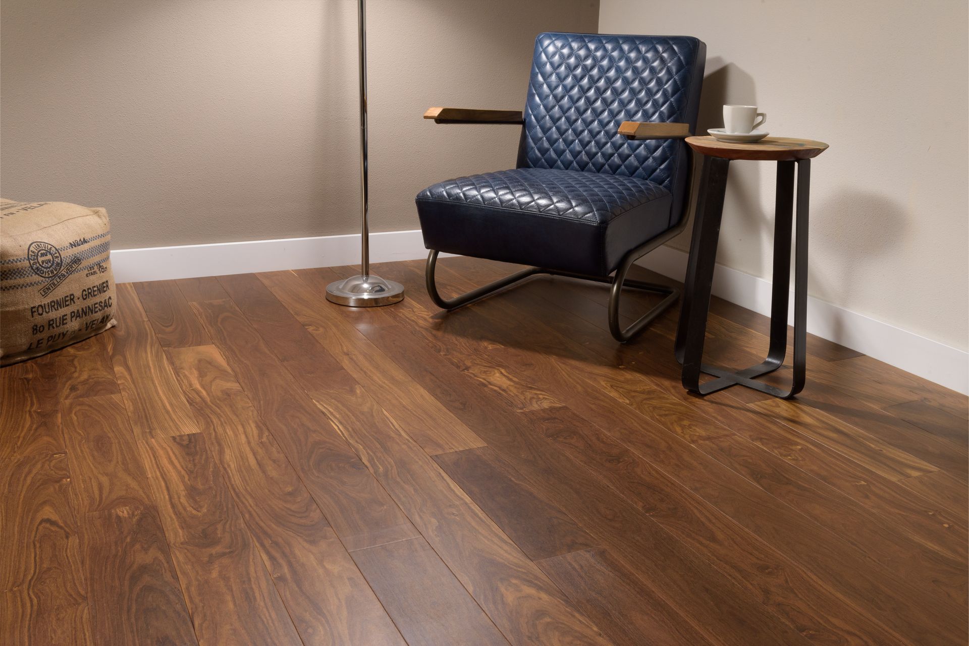 Pièce avec parquet, fauteuil en cuir, petite table avec une tasse, lampadaire.