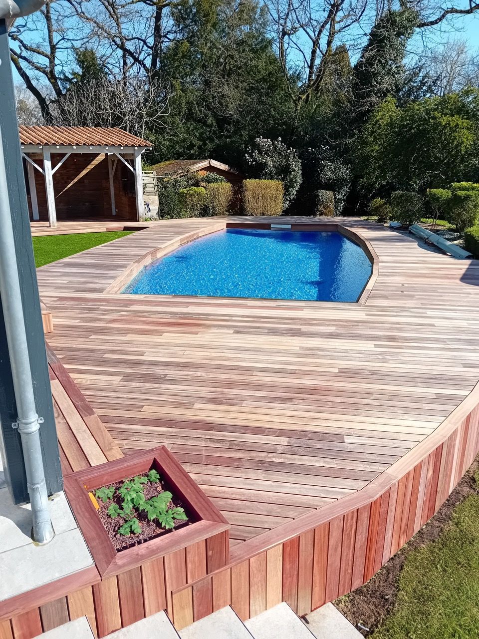 Piscine avec terrasse en bois et petit jardin dans un cadre de cour arrière.