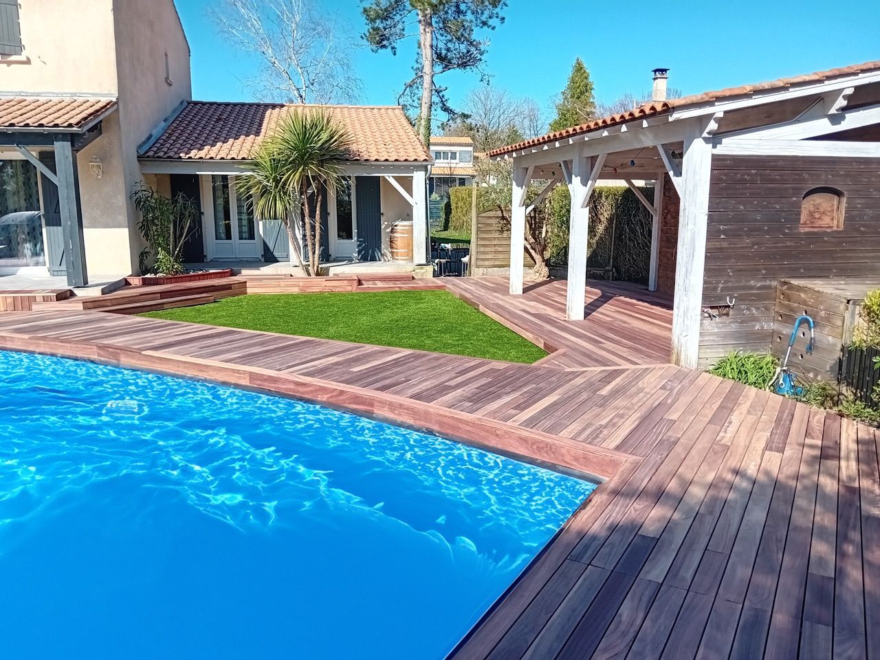 Piscine avec terrasse en bois et maison en arrière-plan.