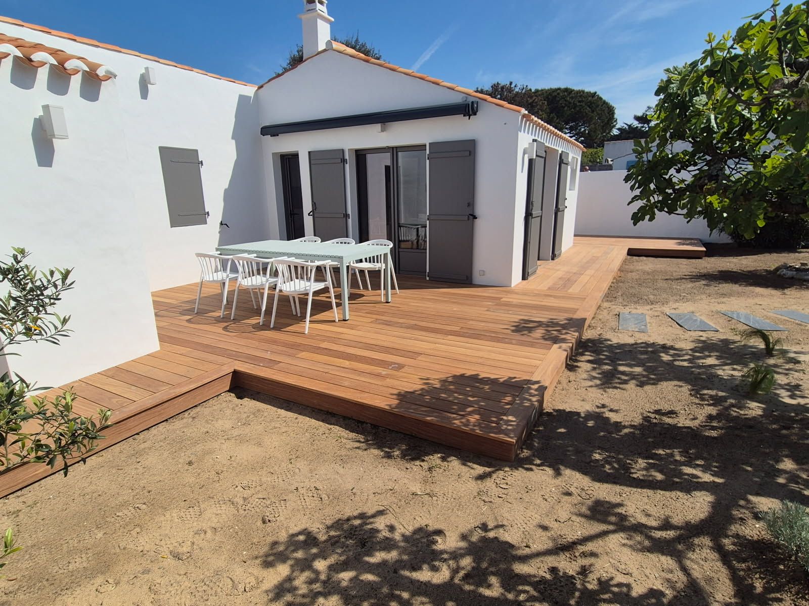 Maisonnette blanche avec terrasse en bois et table à manger extérieure.