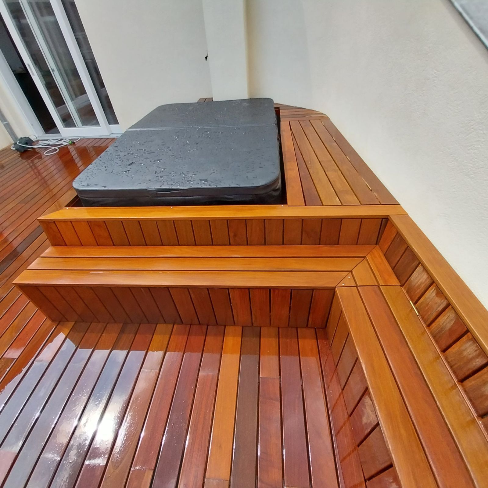 Bain à remous en bois avec marches et couvercle, installé sur une terrasse en bois à côté d'un mur blanc.