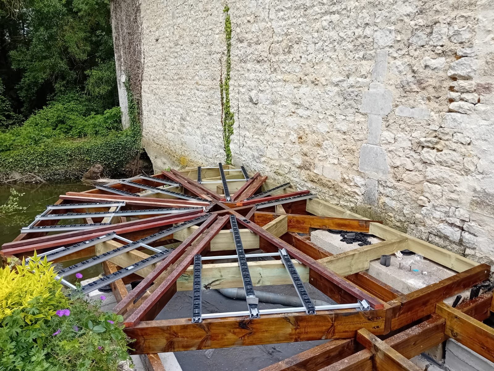 Terrasse en bois en construction à côté d'un mur en pierre.