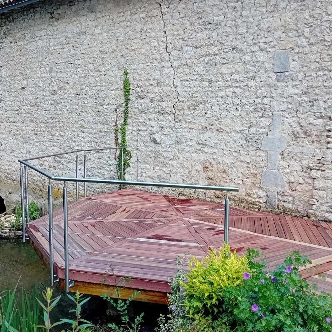 Terrasse en bois avec rambarde métallique, devant un mur de pierre.