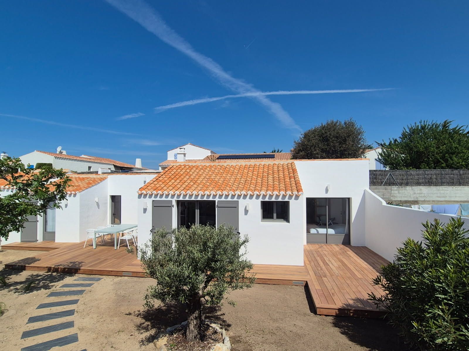Maison en stuc blanc avec toit de tuiles orange et terrasses en bois.