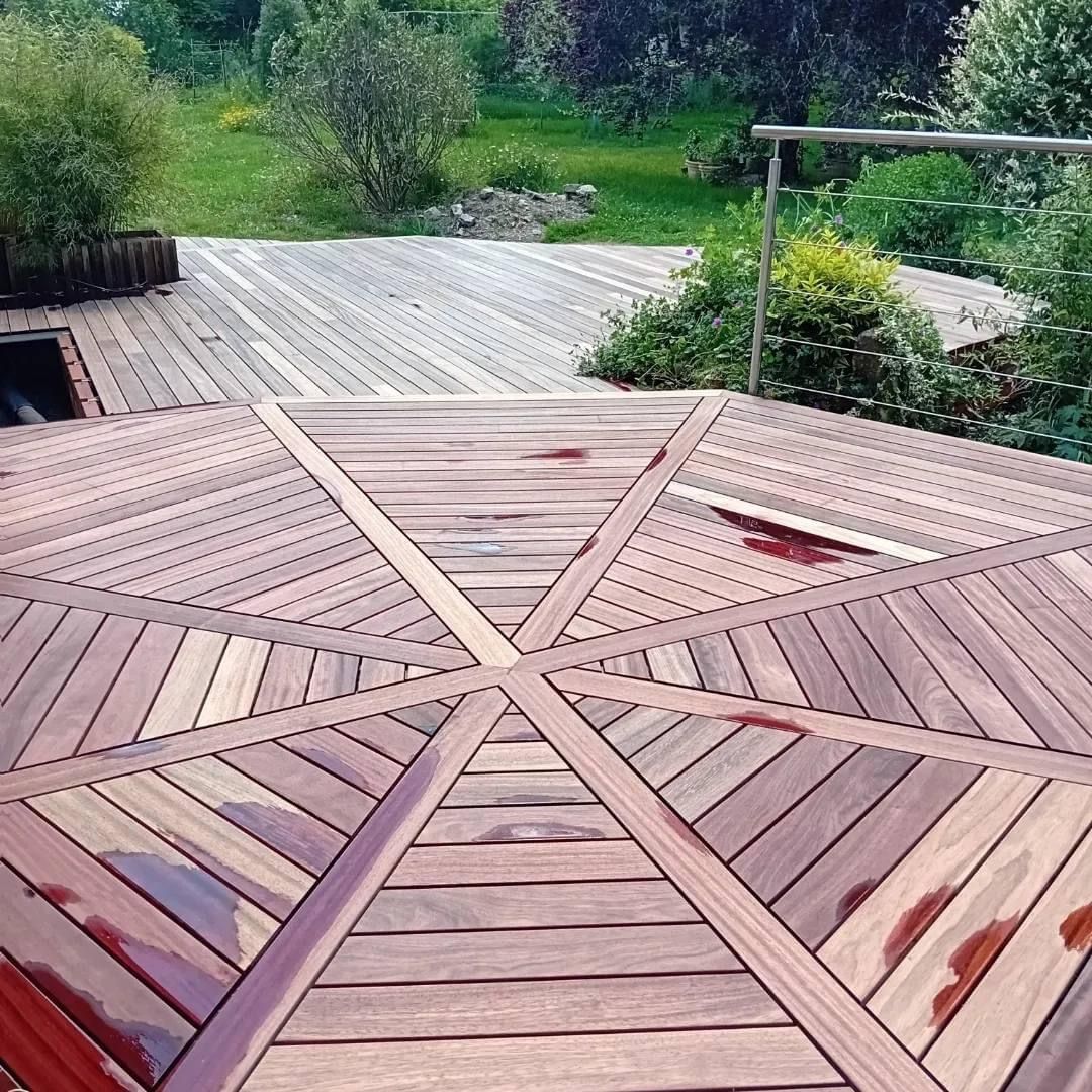 Terrasse en bois au design géométrique, donnant sur une zone herbeuse.