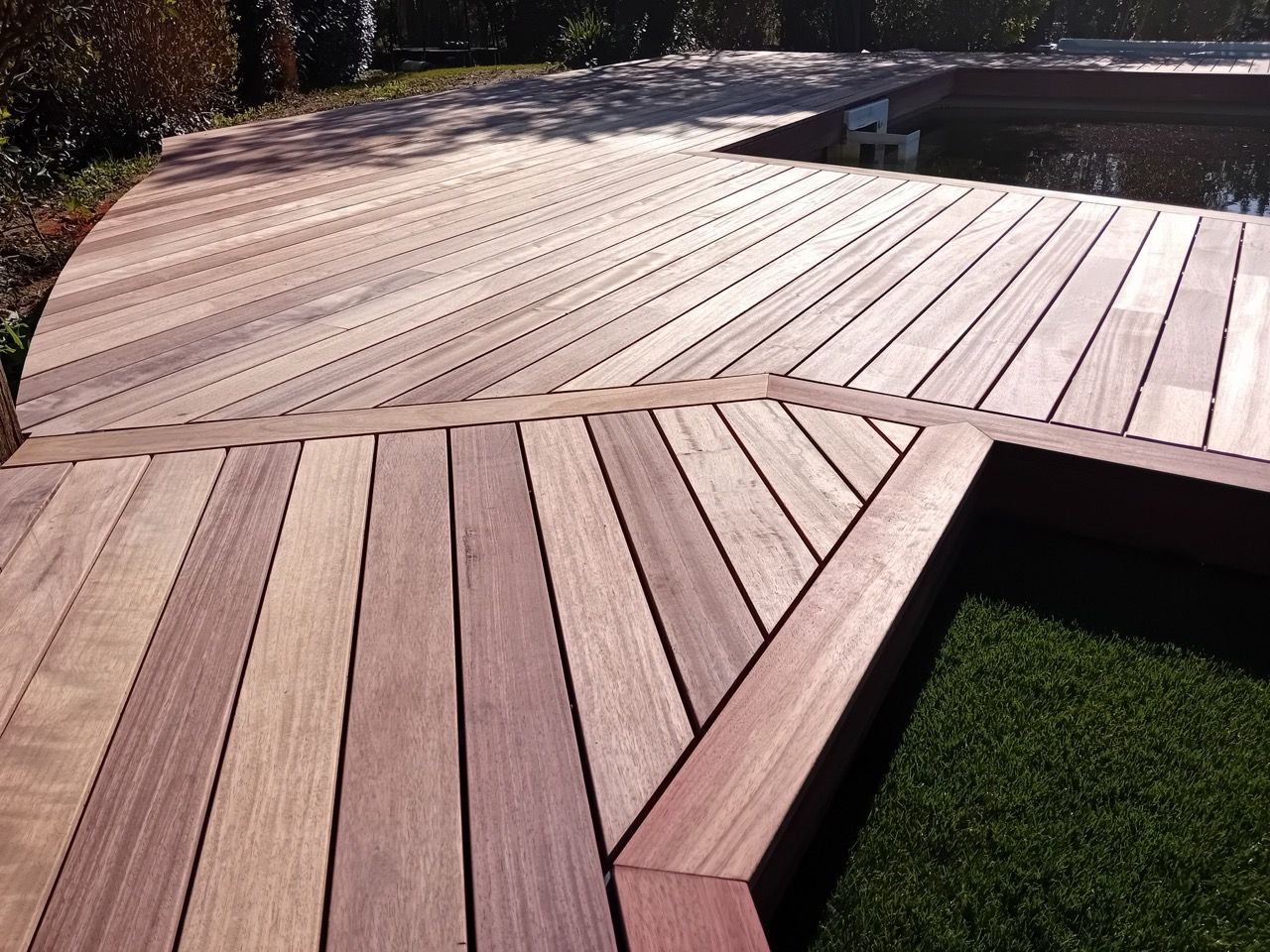 Terrasse en bois aux bords arrondis et au design angulaire, bordée de pelouse verte.