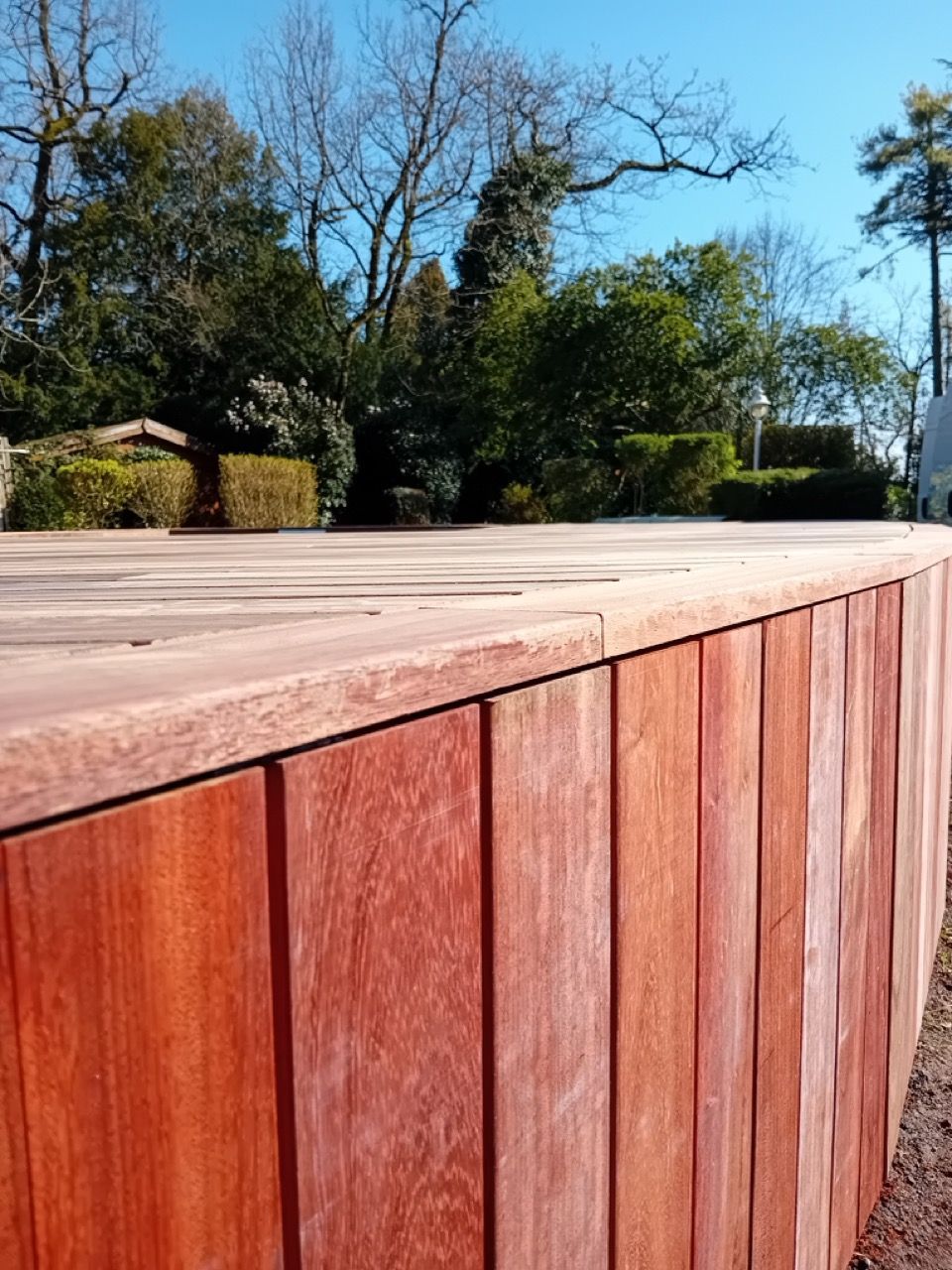 Terrasse en bois aux planches brun rougeâtre, entourée d'un mur vertical de couleur similaire.