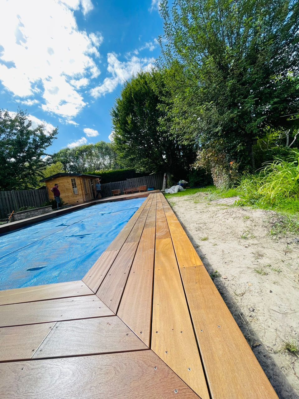 Terrasse en bois bordant une piscine recouverte d'une bâche bleue.