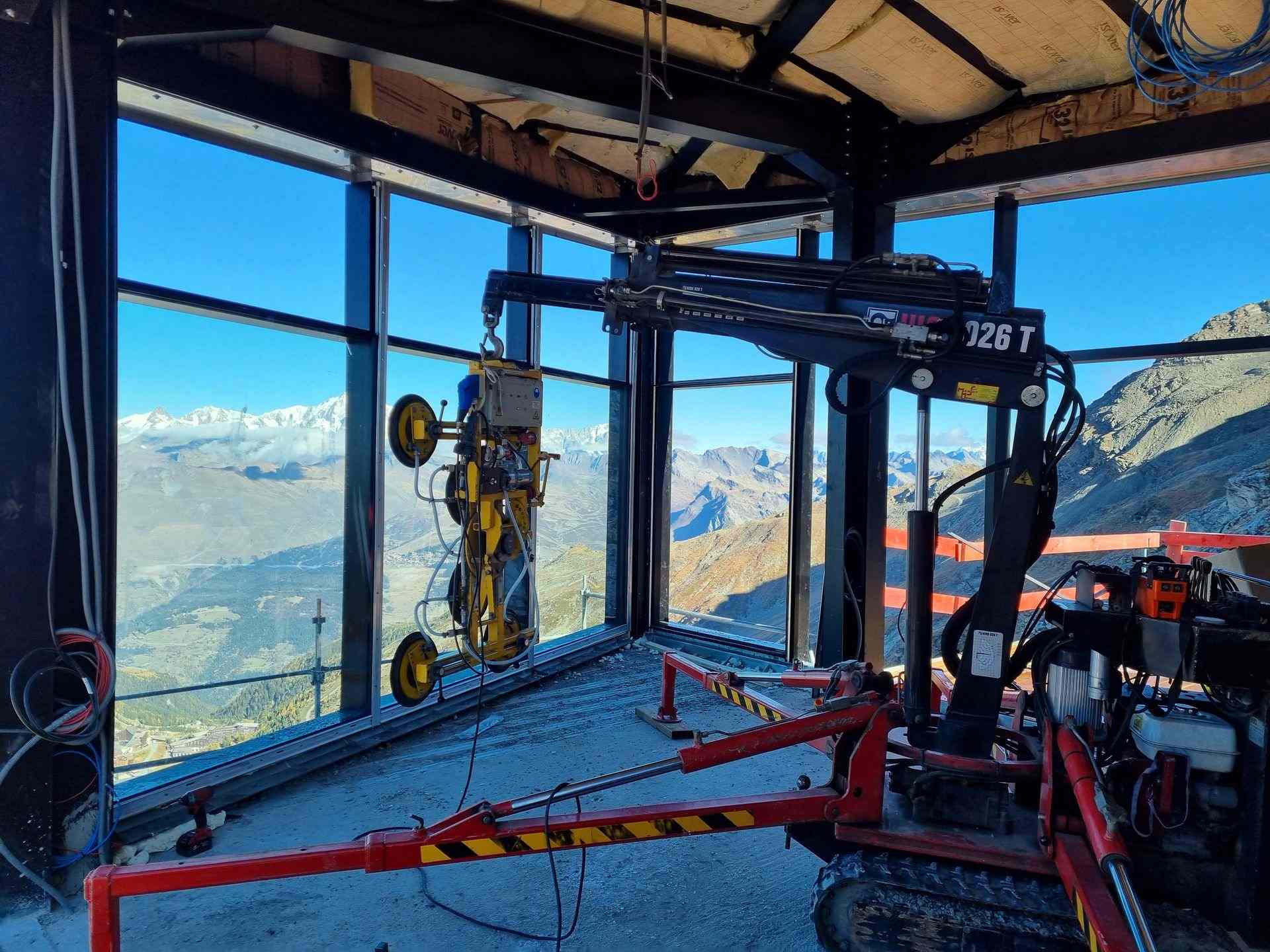 Intérieur d'un bâtiment en chantier sur la pose de vitrage, une grue à quatre ventouse transporte une vitre