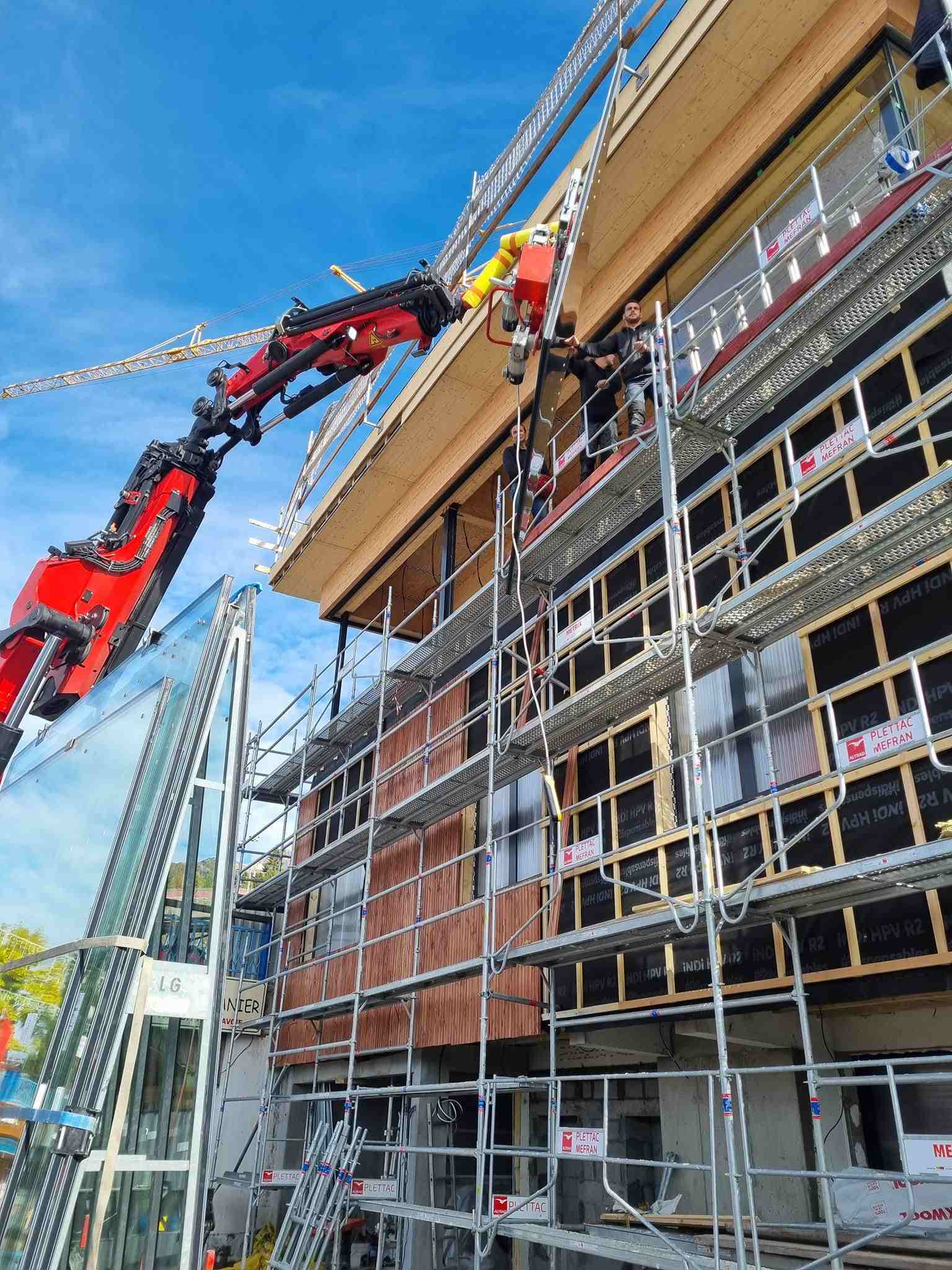Une grue transportant une vitre à un technicien au troisième étage d'un immeuble