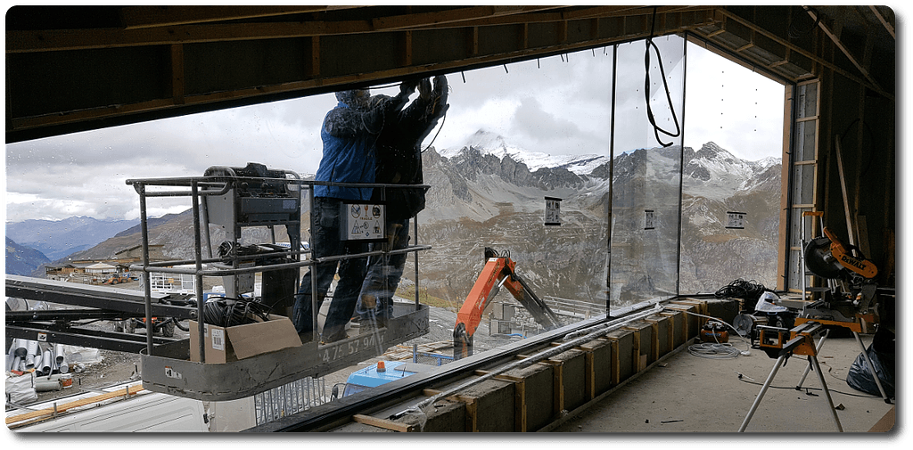 Chantier sur façade vitrée à d'un bâtiment donnant une vue sur une montagne
