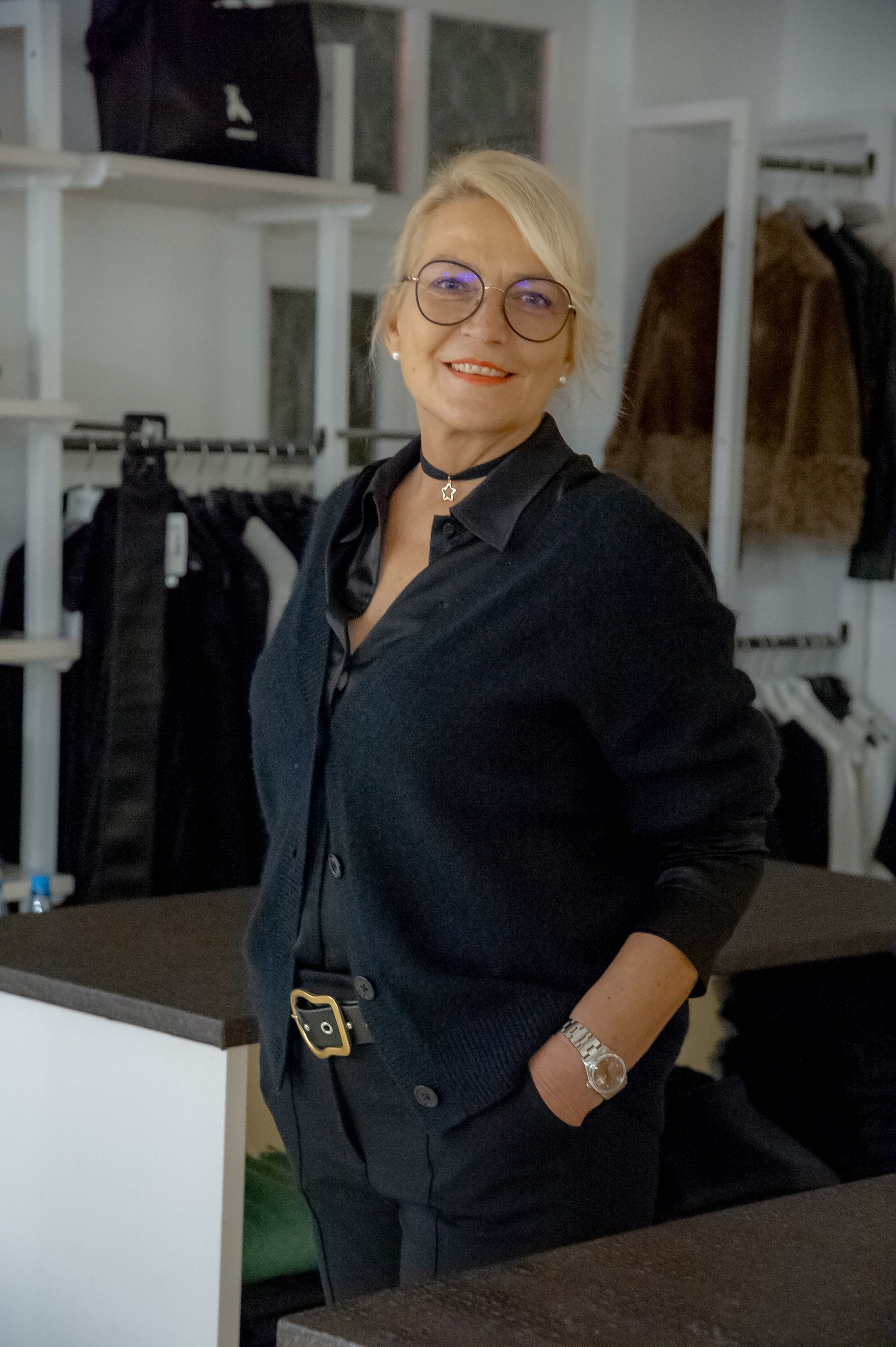 Eine Frau mit Brille steht vor einem Schrank voller Kleidung.