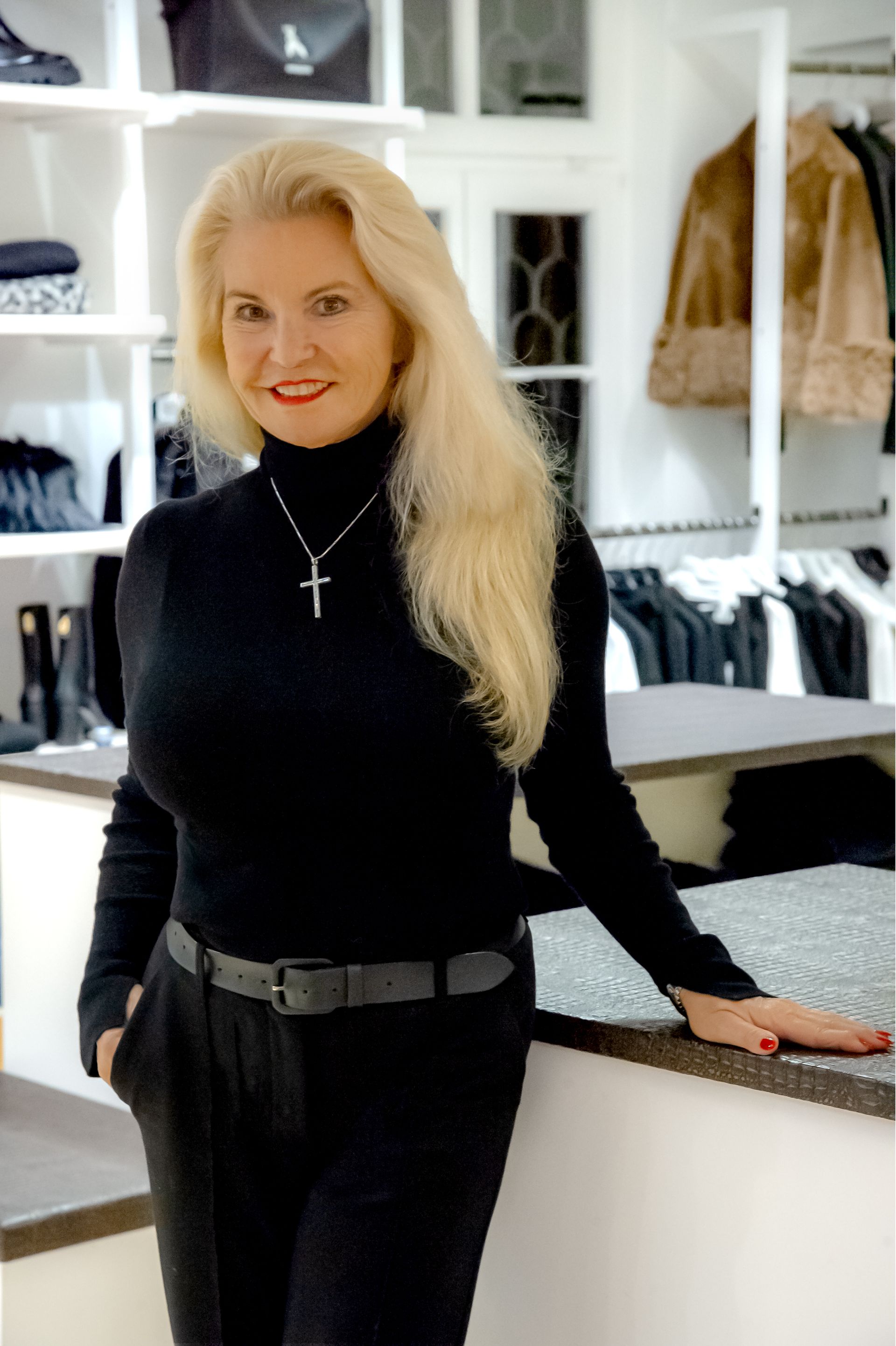 Eine Frau in einem schwarzen Hemd und einem schwarzen Rock steht vor einem Kleiderständer.