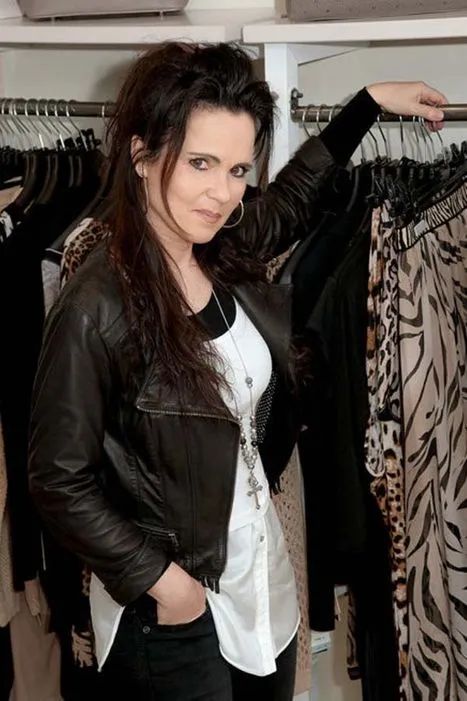 Eine Frau in einer Lederjacke steht vor einem Schrank voller Kleidung.