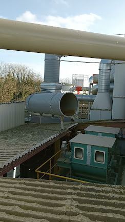 Tuyaux et conduits industriels au-dessus d’un bâtiment doté d’une toiture végétalisée, sous un ciel nuageux