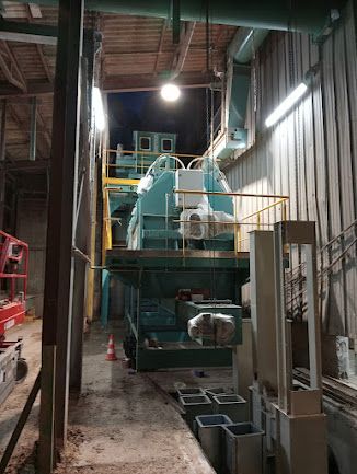 Machine industrielle dans une allée d’entrepôt sombre, avec des équipements verts et un éclairage au plafond