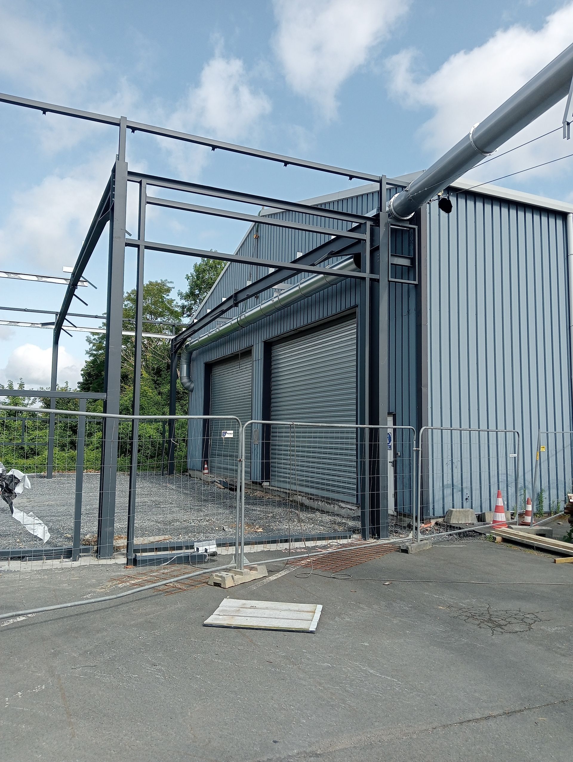 Bâtiment industriel avec un bardage métallique bleu-gris, derrière une clôture en grillage et sur un terrain de gravier