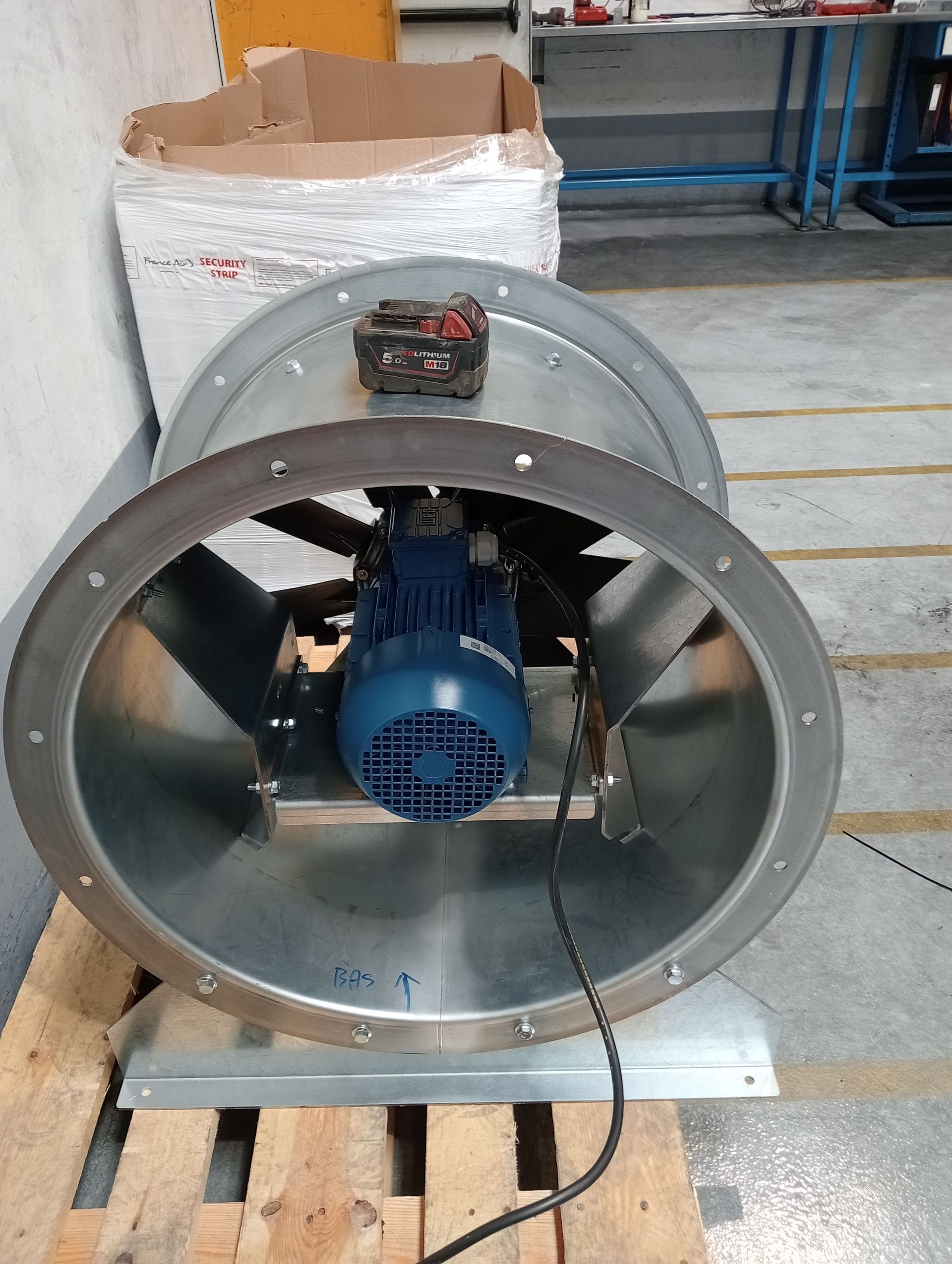 Ventilateur de ventilation industrielle à l’intérieur d’un grand conduit métallique, posé sur une palette en bois.