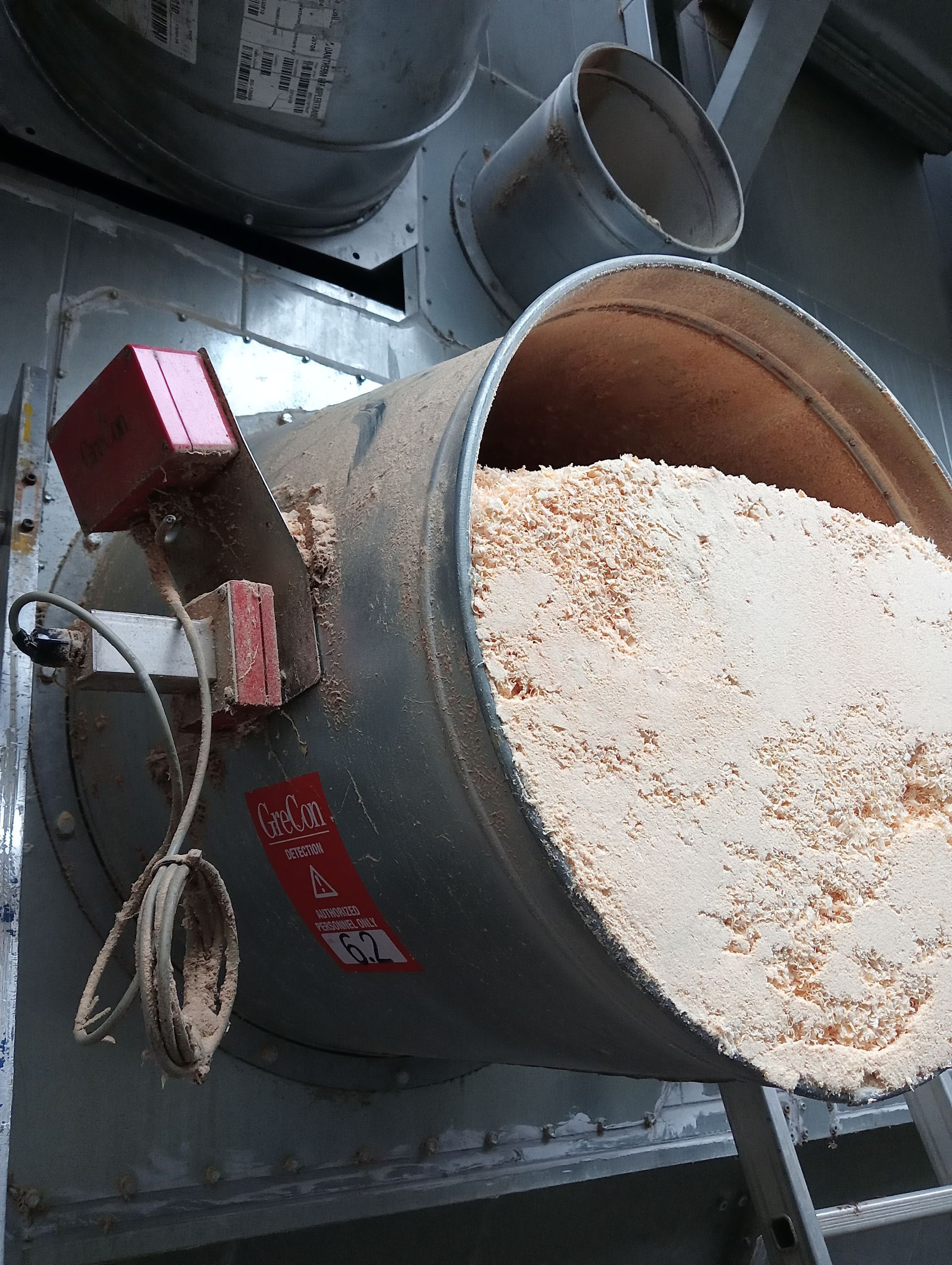 Gros plan sur une trémie industrielle grise équipée d’un moteur rouge, remplie de poudre blanche et de particules de rouille.