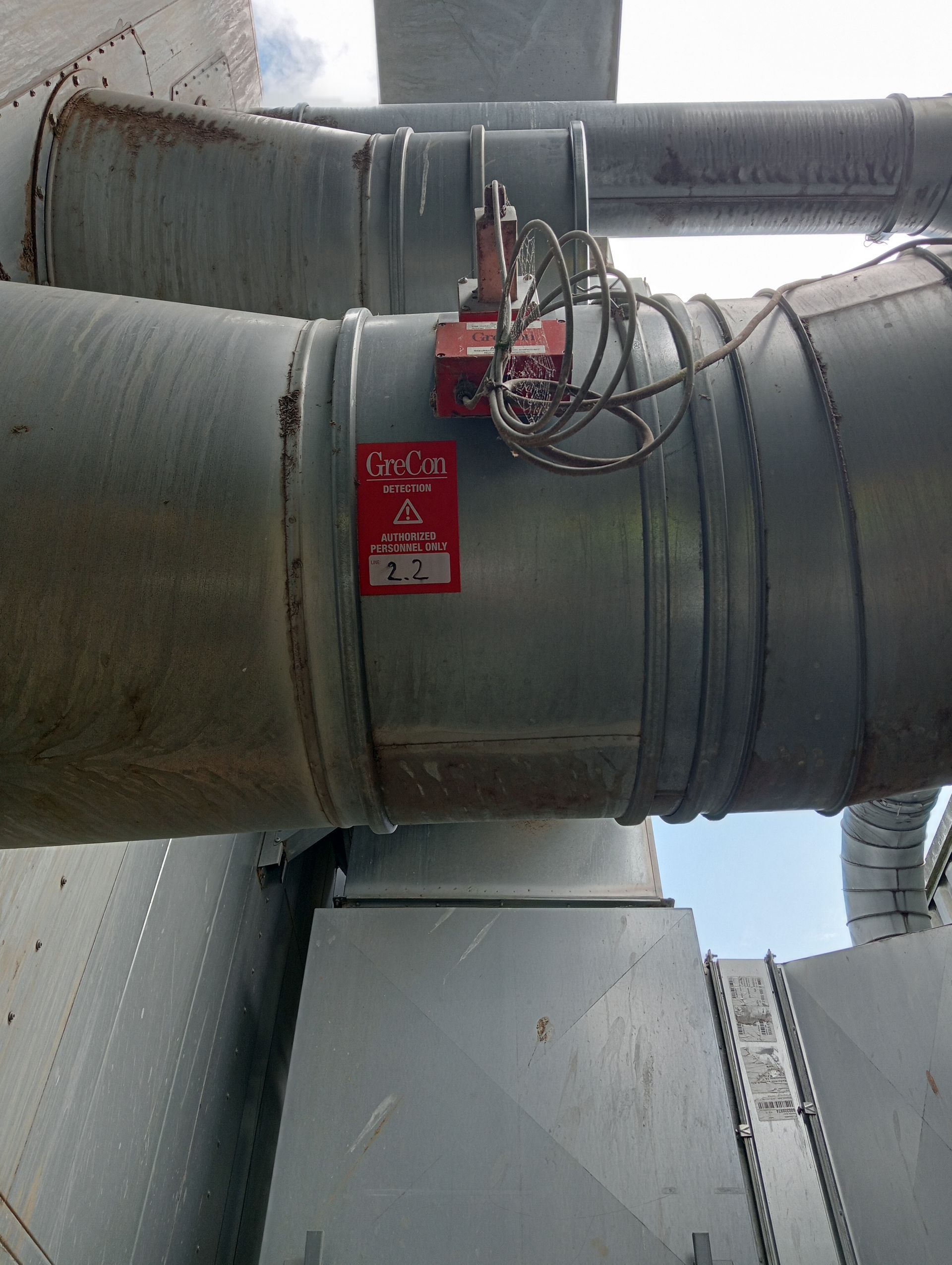 Gros conduit industriel avec un panneau d’avertissement rouge et des câbles fixés dans une salle des machines