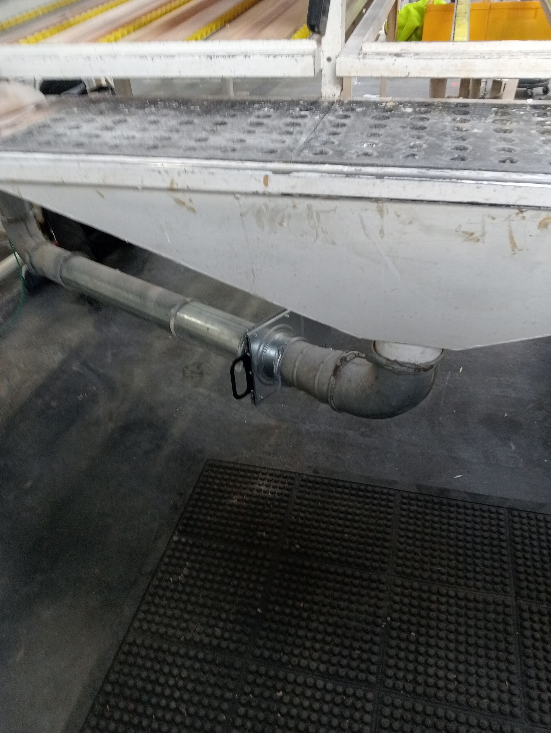 Tuyau endommagé dépassant sous une plateforme métallique dans une zone industrielle, avec un seau fixé pour recueillir les gouttes