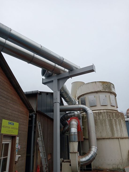 Des tuyaux et des équipements industriels à côté d’un bâtiment en briques et de réservoirs rouillés, à l’extérieur