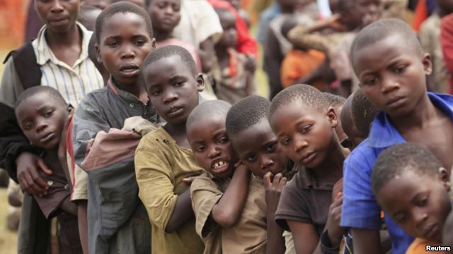 Mehrere Kinder stehen im Freien dicht beieinander, einige lehnen sich aneinander, mit ernsten Gesichtsausdrücken.