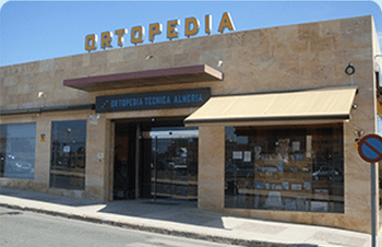 Fachada de ORTOPEDIA, un edificio de color beige con un toldo a rayas y grandes ventanales.
