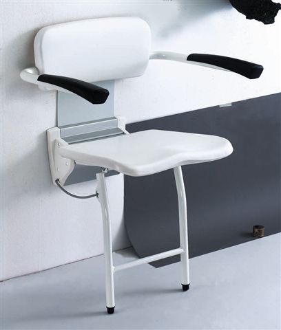 Silla de ducha blanca montada en la pared con reposabrazos negros y patas plegables en un baño.