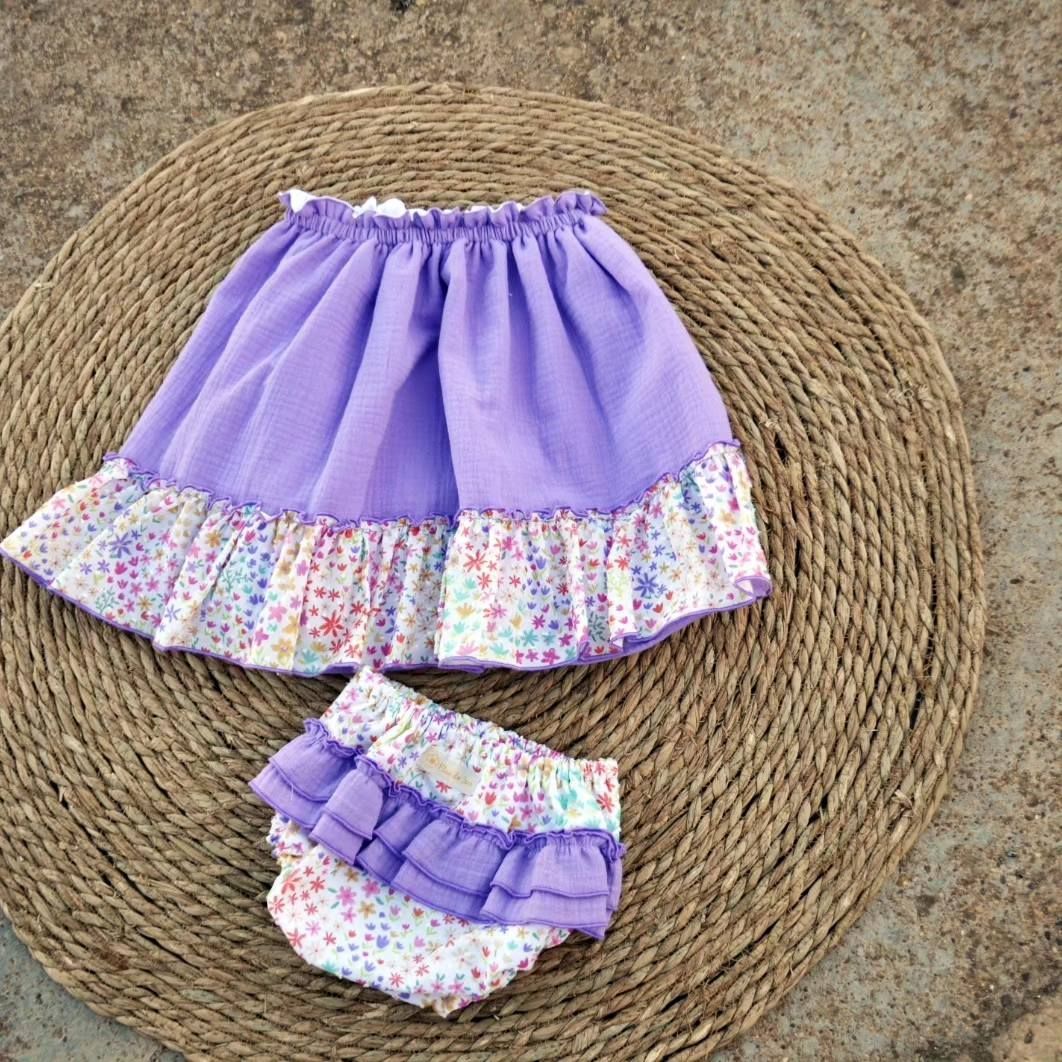 Una falda morada y un pañal están sobre una estera de mimbre.