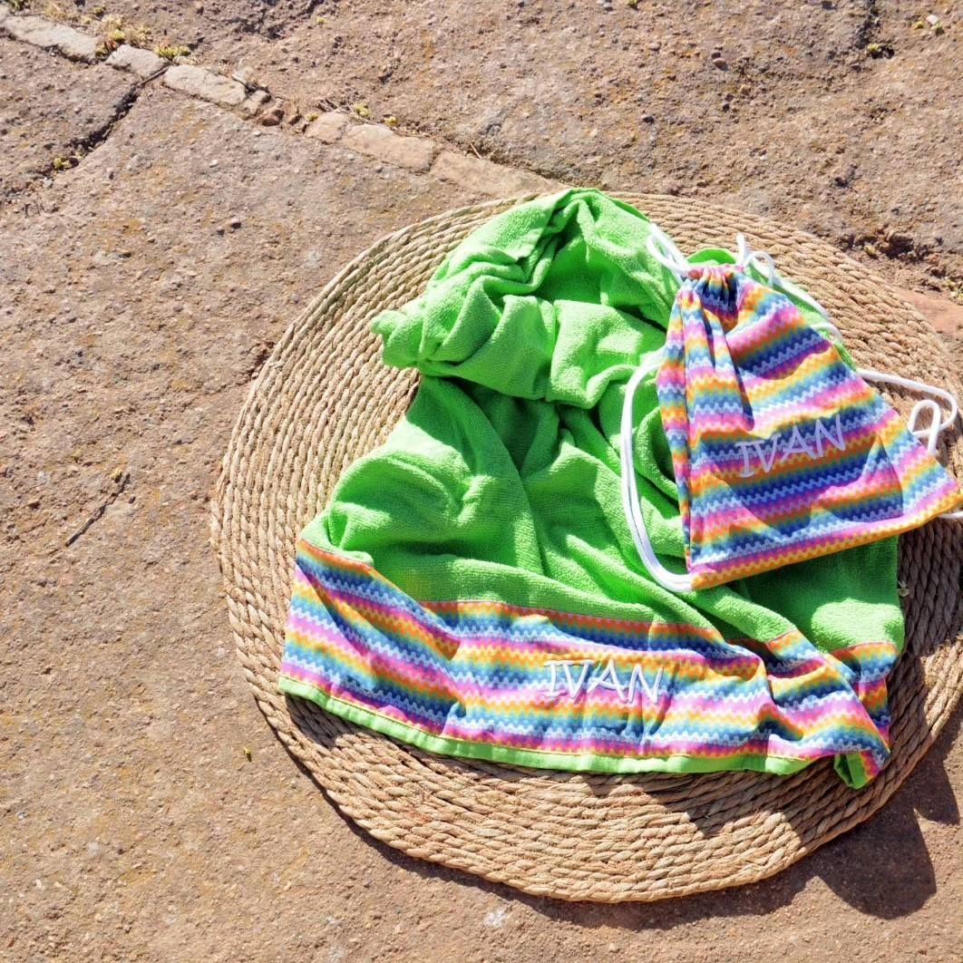 Una toalla verde y una bolsa con rayas de arcoíris están sobre una estera de mimbre.