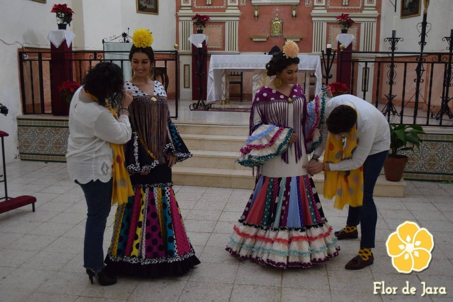 Una mujer con un vestido colorido está siendo ayudada por un hombre con un logo de flor de jara