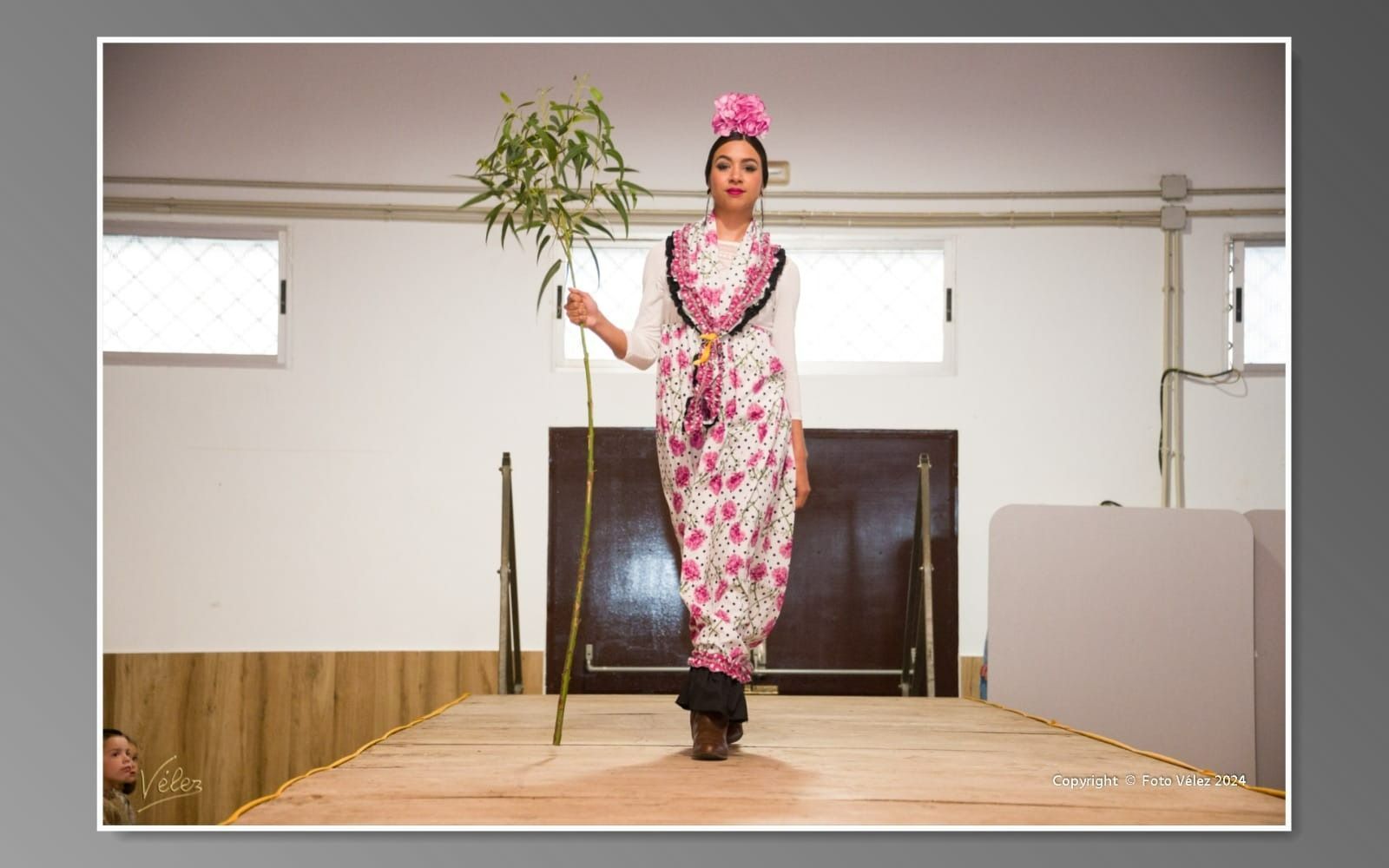 Una mujer con un vestido floral camina por una pasarela sosteniendo una planta.