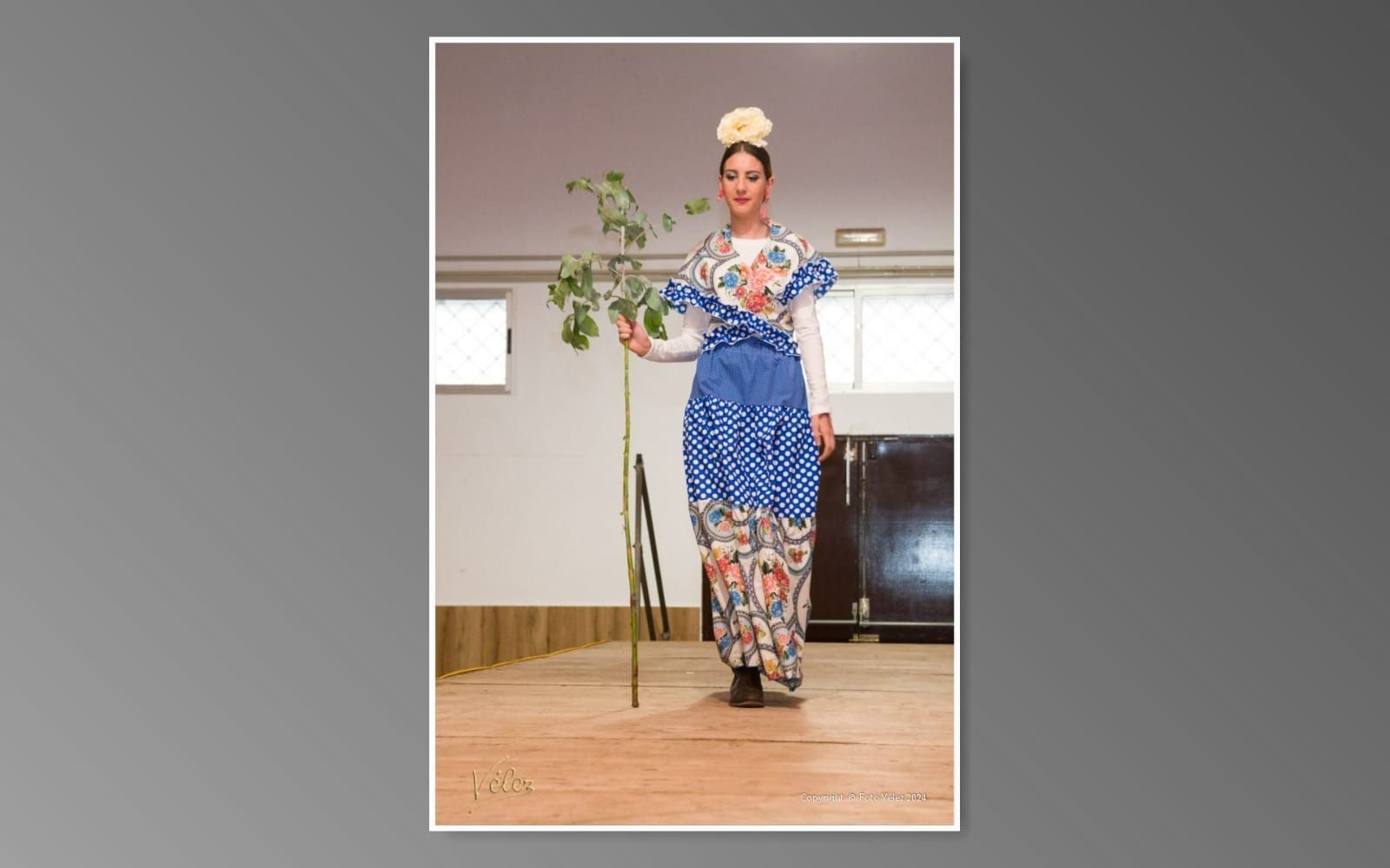Una mujer con un vestido azul y blanco sostiene una flor.