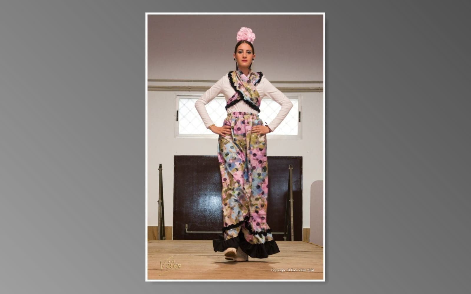 Una mujer con un vestido floral está parada en una habitación con las manos en las caderas.