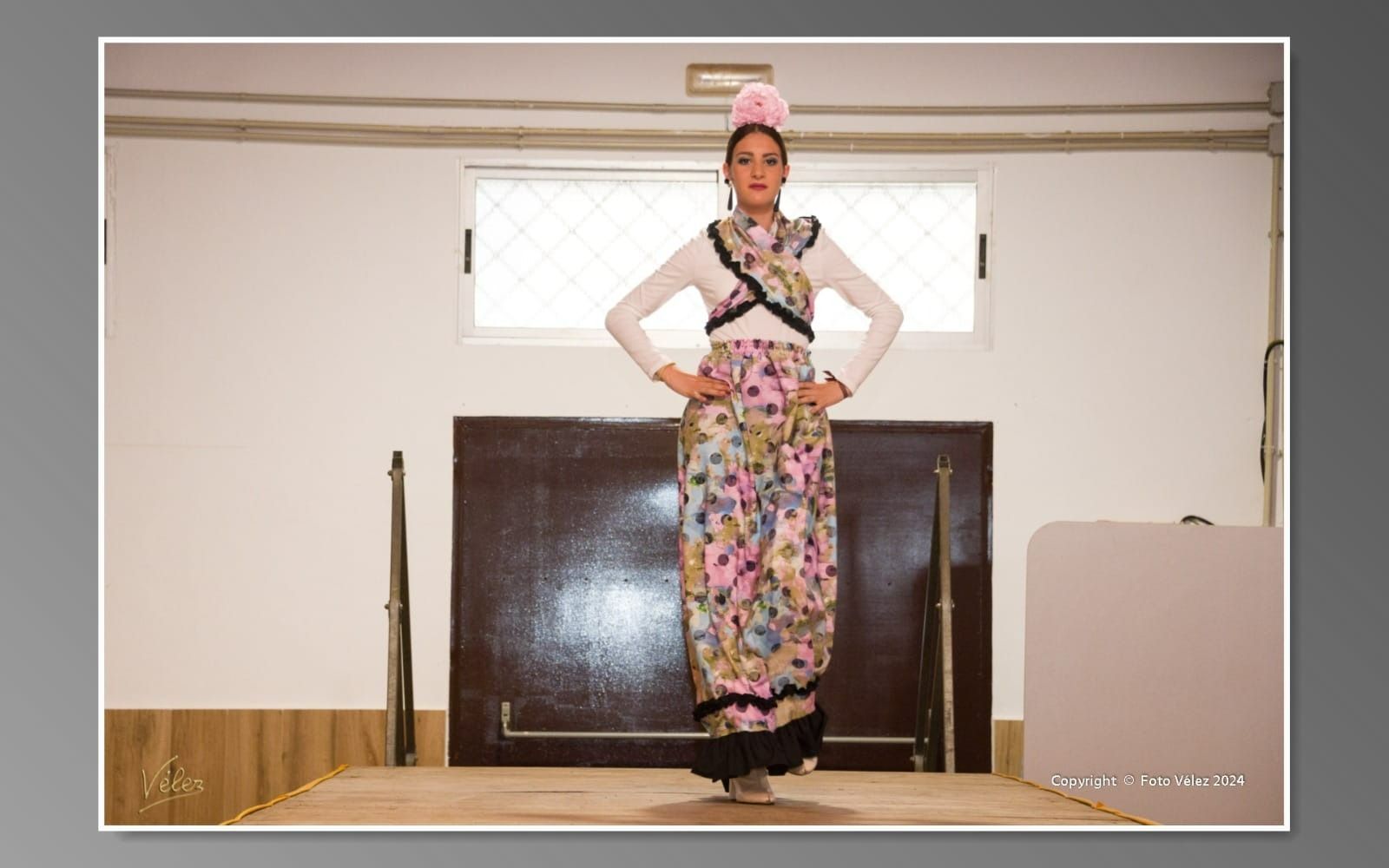 Una mujer con un vestido floral está de pie en una habitación con las manos en las caderas.