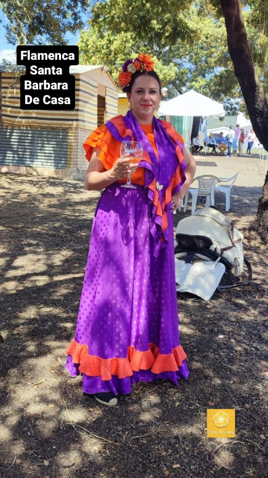 Una mujer con un vestido morado y naranja sostiene una copa de vino.