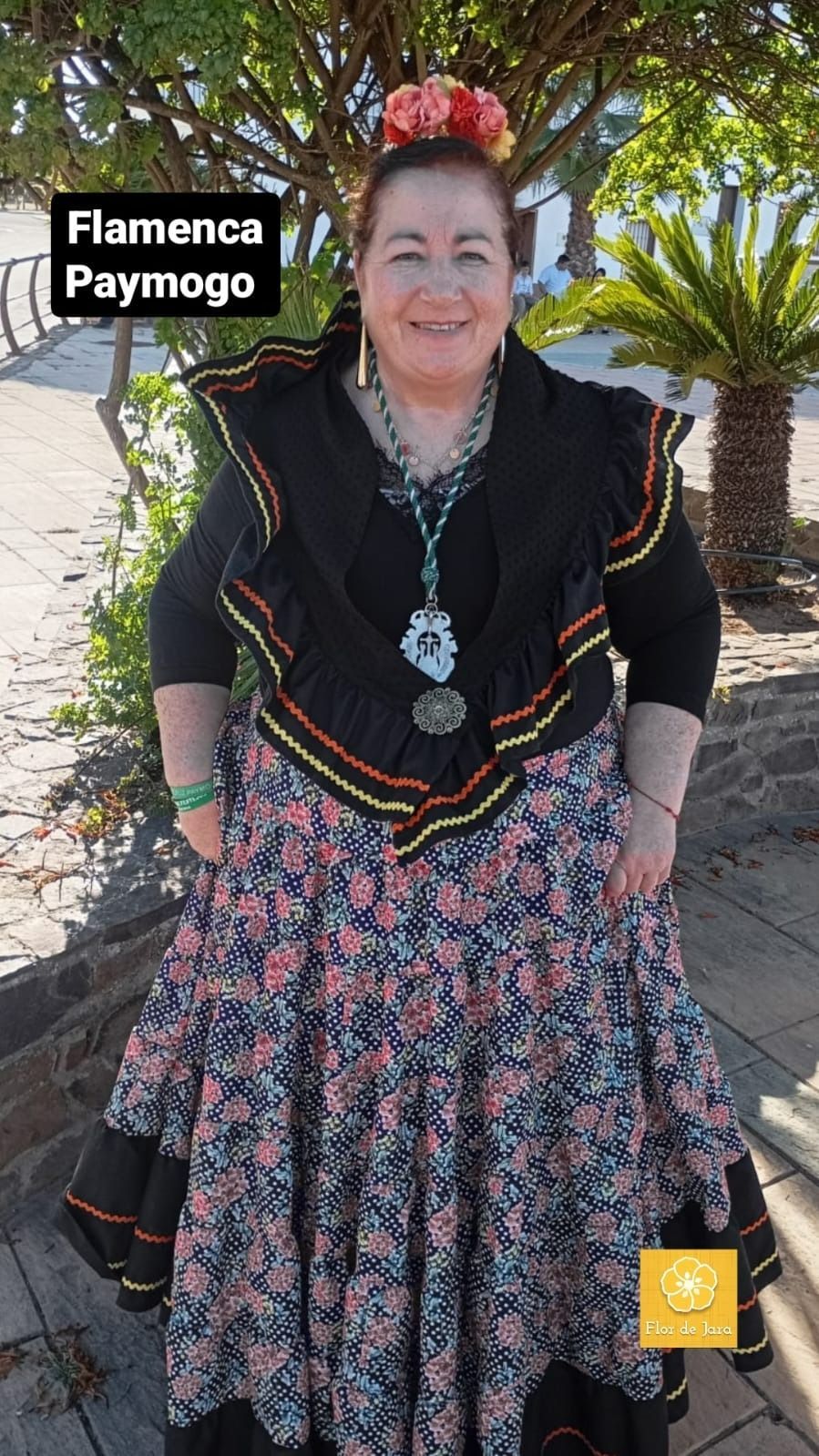 Una mujer con un vestido de flamenca está parada frente a un árbol.