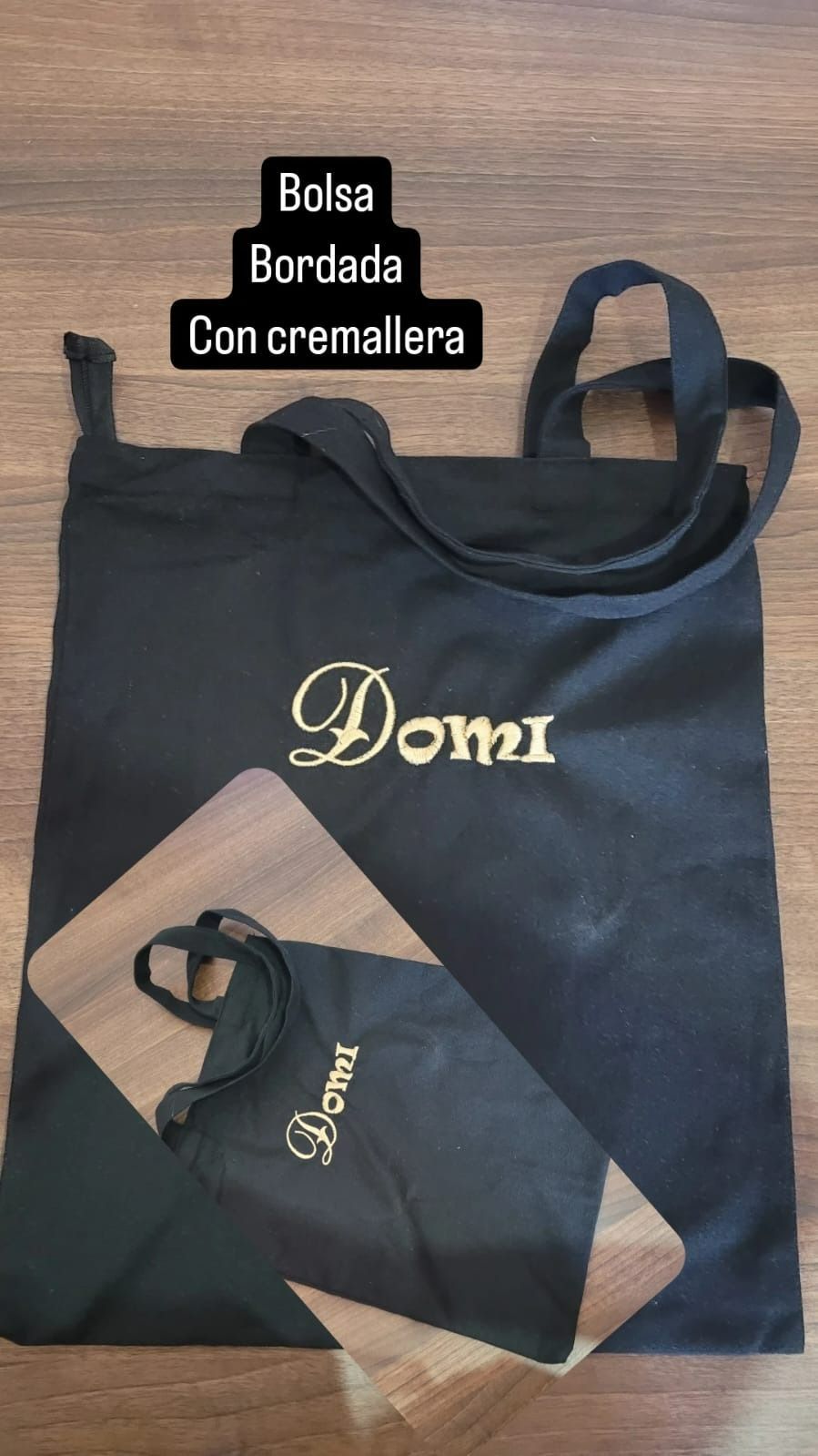 Una bolsa de mano negra con el nombre Domi bordado está sobre una mesa de madera.