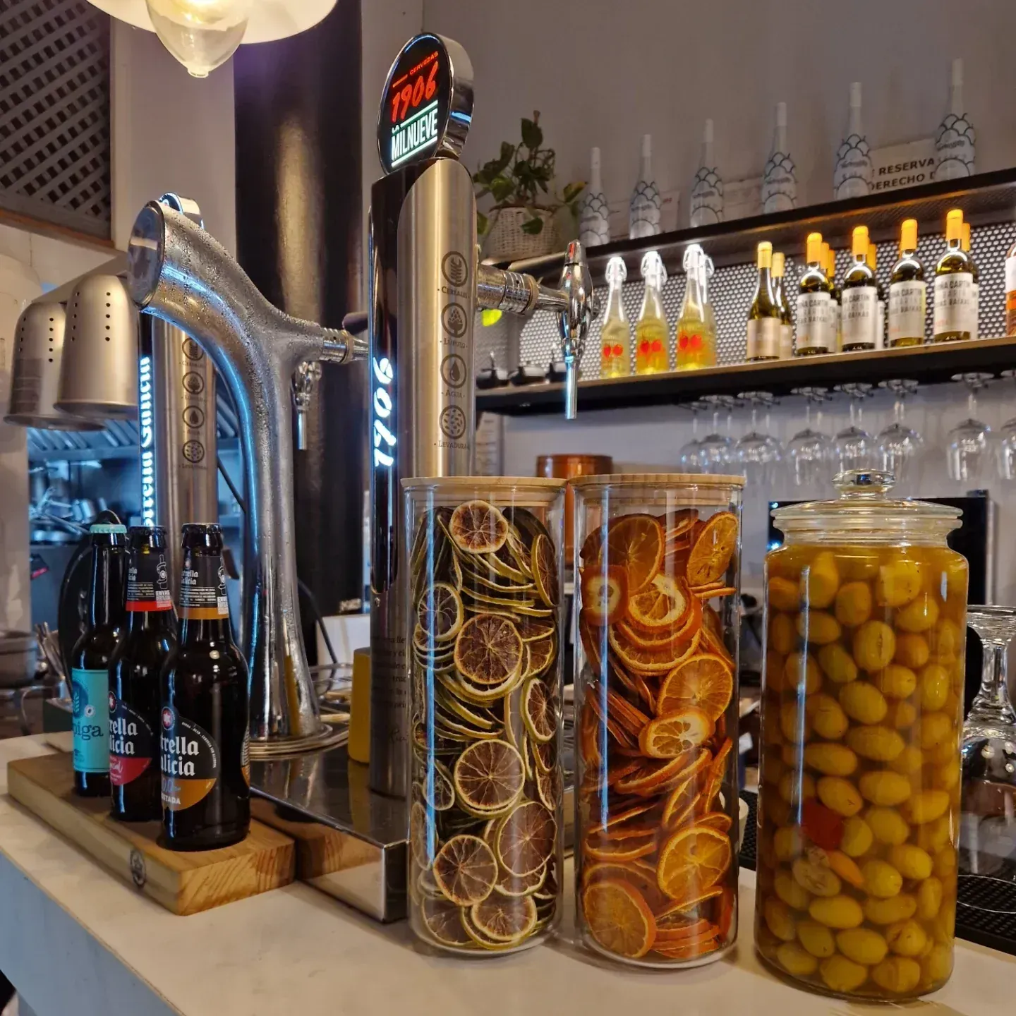 Barra de bar con grifos de cerveza, cerveza embotellada, tarros de cristal con cítricos secos y aceitunas.