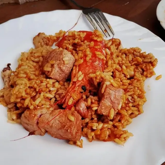 Plato de arroz rojizo con trozos de carne y un tenedor en un plato blanco.