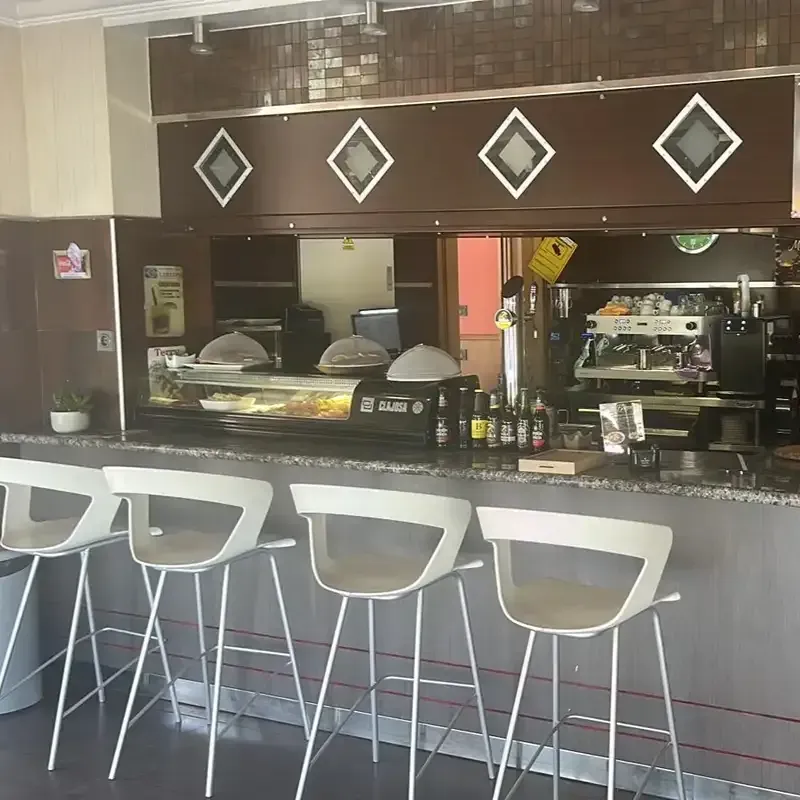 Barra de cafetería moderna con taburetes blancos y una vitrina de cristal para pasteles bajo una decoración de pared.