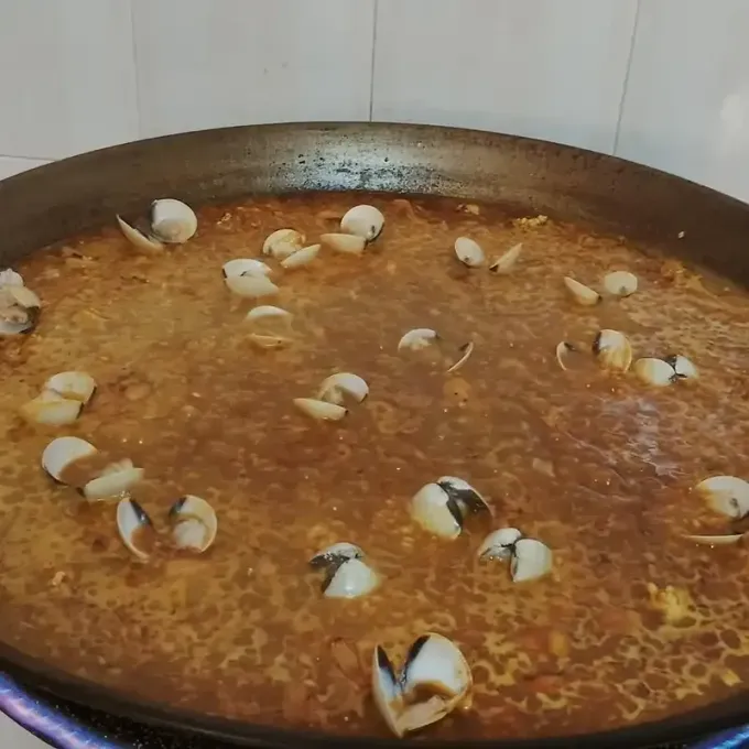 Una olla grande con salsa de naranja hirviendo a fuego lento, cubierta con mariscos esparcidos, sobre una estufa.