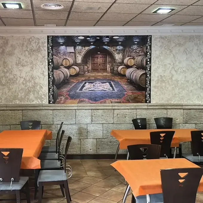 Comedor del restaurante con manteles naranjas, sillas negras y un mural de un viñedo en la pared.
